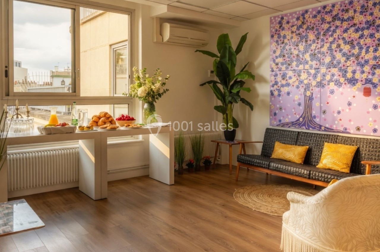 Salon lumineux avec parquet, canapé, fauteuil, plantes, tableau coloré et table dressée près d'une fenêtre donnant sur des…