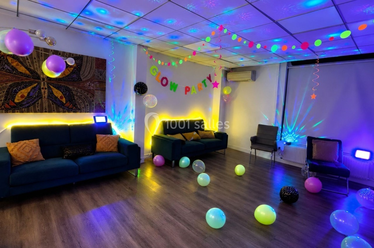 Salle décorée pour une fête fluorescente avec ballons, guirlandes lumineuses et néons colorés.