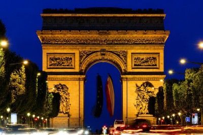 Vue nocturne de l'Arc de Triomphe illuminé, entouré de circulation et d'arbres sur les Champs-Élysées.