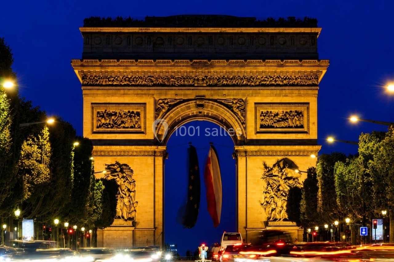 Vue nocturne de l'Arc de Triomphe illuminé, entouré de circulation et d'arbres sur les Champs-Élysées.