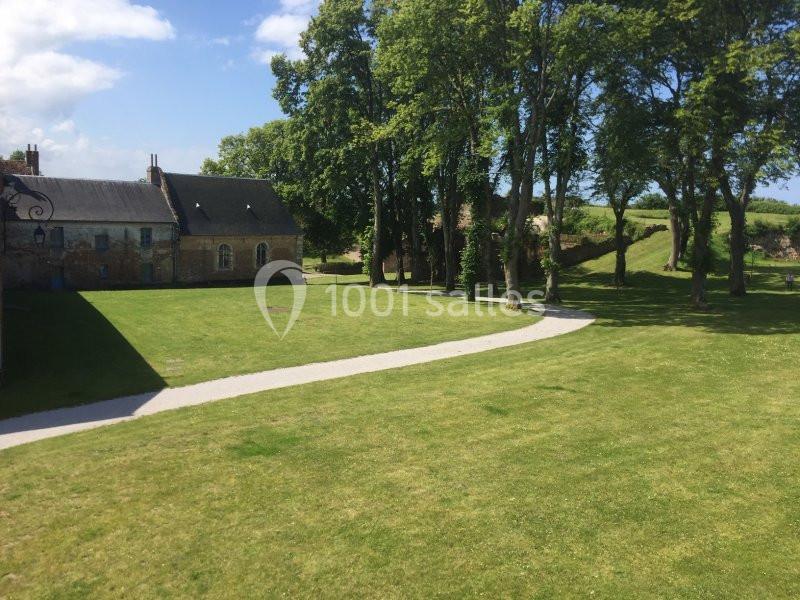 Chemin sinueux traversant une pelouse verdoyante bordée d'arbres et de bâtiments en pierre sous un ciel bleu.