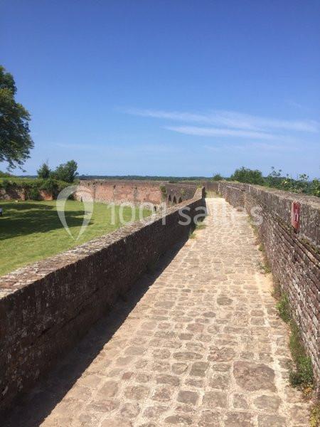 Chemin pavé longeant un mur de briques avec vue sur un espace vert et un ciel dégagé.