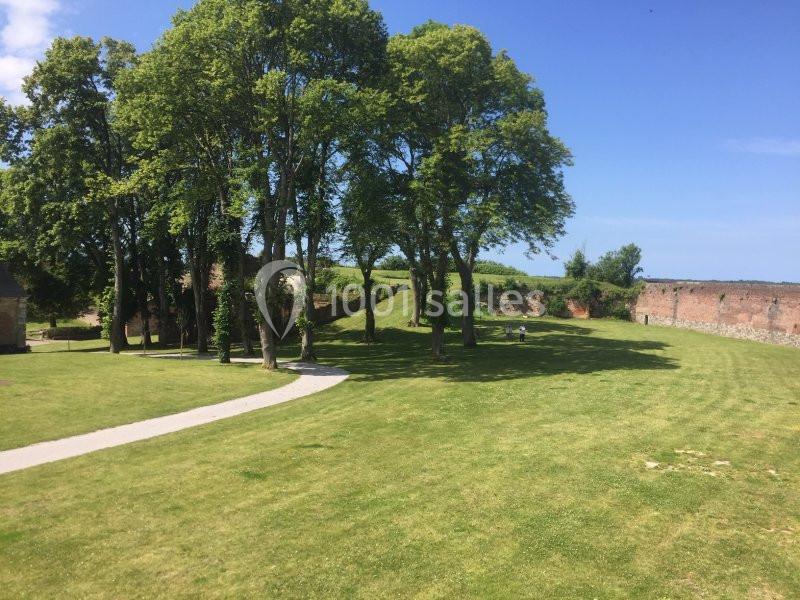 Pelouse verdoyante bordée d'arbres et de murs en briques sous un ciel bleu dégagé.
