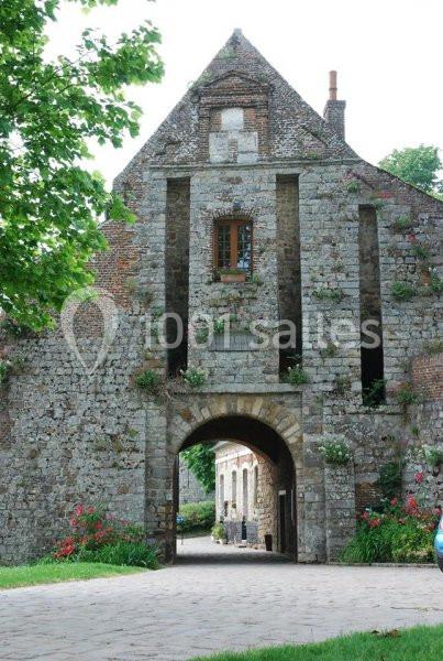 Vieille porte en pierre avec un arc voûté, entourée de murs anciens et de végétation fleurie.