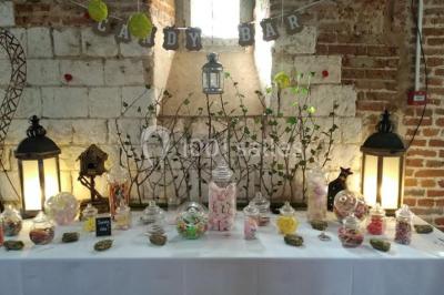 Des bancs en bois disposés en extérieur, entourés de décorations végétales, avec des arbres et des bâtiments en arrière-plan.