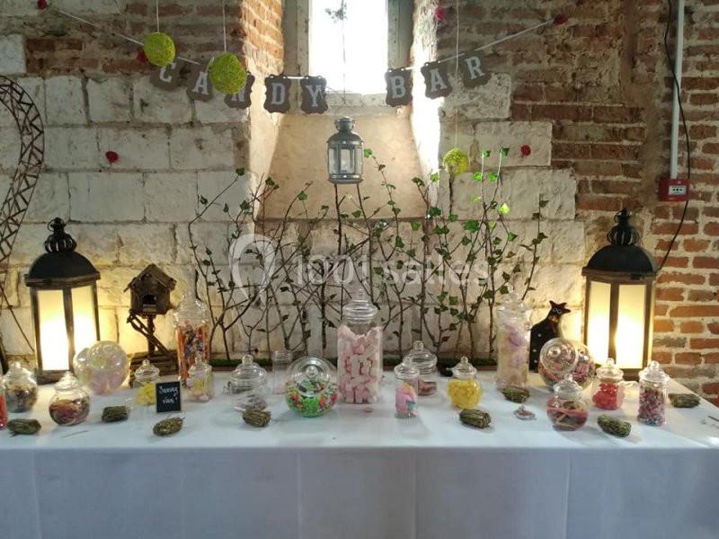 Table décorée avec des bonbonnières remplies de confiseries variées, éclairée par deux lanternes et une lumière naturelle.