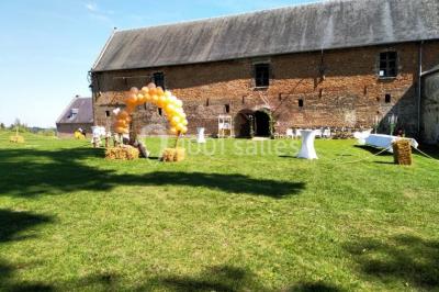 Des bancs en bois disposés en extérieur, entourés de décorations végétales, avec des arbres et des bâtiments en arrière-plan.