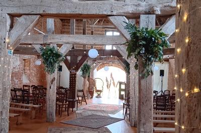 Des bancs en bois disposés en extérieur, entourés de décorations végétales, avec des arbres et des bâtiments en arrière-plan.