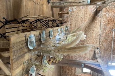 Des bancs en bois disposés en extérieur, entourés de décorations végétales, avec des arbres et des bâtiments en arrière-plan.