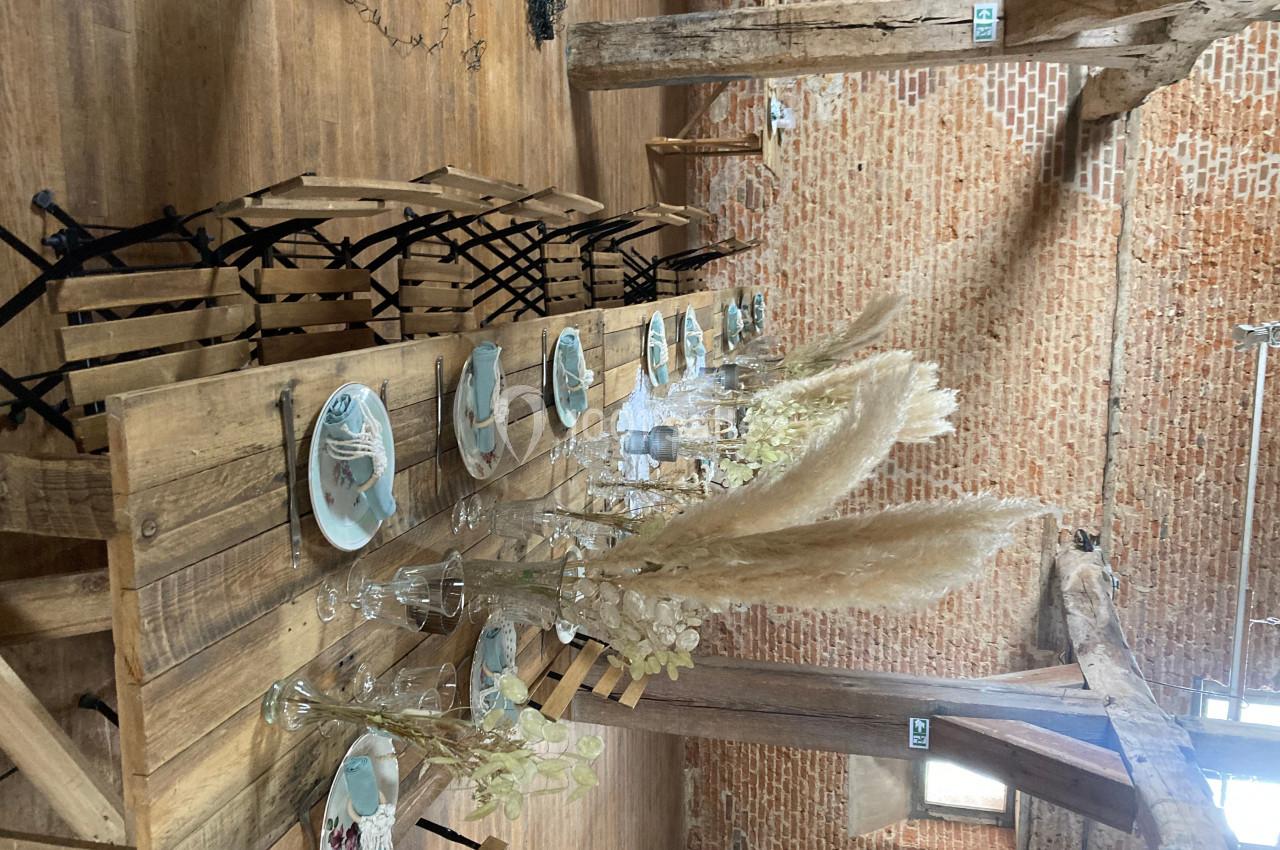 Table en bois rustique dressée avec vaisselle et décorations naturelles, dans une salle aux murs en briques et poutres…