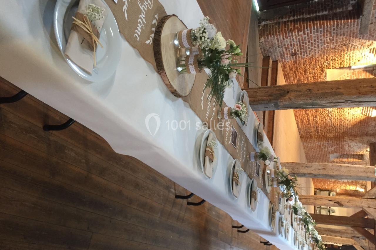 Table de réception décorée avec des fleurs blanches, nappes blanches, chemins de table en jute et vaisselle disposée.