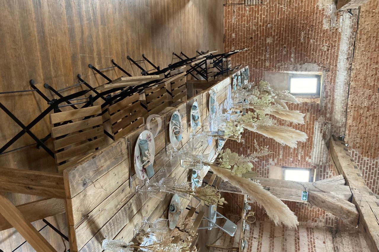 Table en bois décorée avec des assiettes, verres et bouquets de fleurs séchées, dans une salle aux murs en briques…