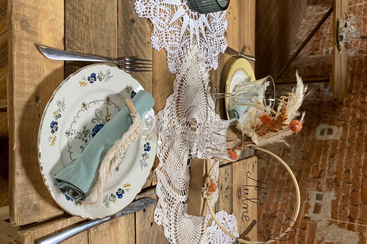 Table en bois décorée avec des assiettes fleuries, un chemin de table en dentelle et des éléments de décoration champêtre.