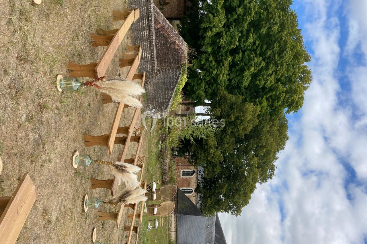 Des bancs en bois disposés en extérieur, entourés de décorations végétales, avec des arbres et des bâtiments en arrière-plan.