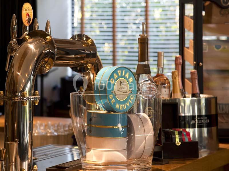 Boîte de caviar posée dans un seau transparent sur un comptoir de bar avec bouteilles et pompe à bière en arrière-plan.