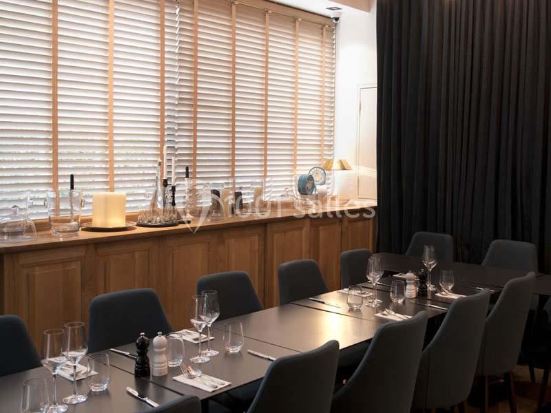 Salle à manger moderne avec table dressée, chaises grises, lumière naturelle filtrée par des stores en bois.