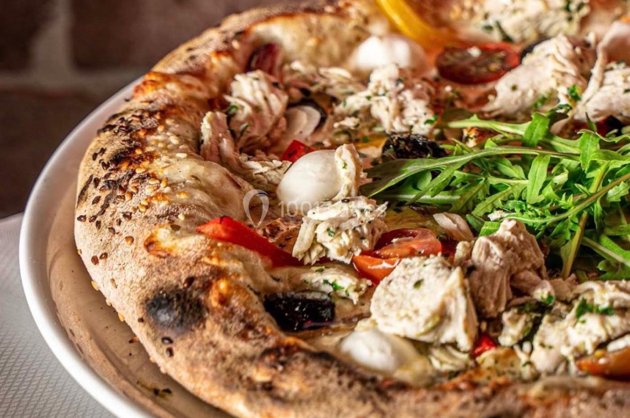 Pizza garnie de morceaux de poulet, roquette, tomates cerises, mozzarella et poivrons sur une pâte dorée.