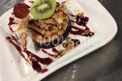 Dessert dressé sur une assiette blanche avec coulis de fruits rouges, tranche de kiwi, chantilly et éclats d'amandes.