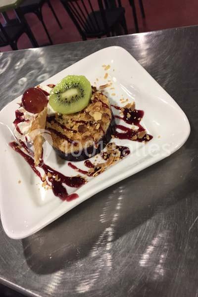 Dessert dressé sur une assiette blanche avec coulis de fruits rouges, tranche de kiwi, chantilly et éclats d'amandes.