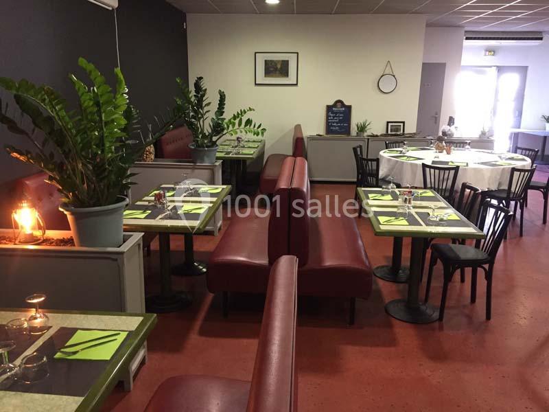 Salle de restaurant avec tables dressées, banquettes rouges, plantes décoratives et lumière naturelle en arrière-plan.