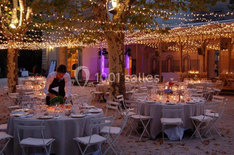 Tables rondes décorées pour un dîner en plein air sous des guirlandes lumineuses, avec un serveur en action.