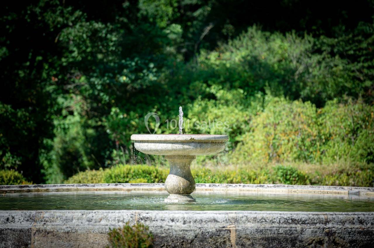 Fontaine en pierre au centre d'un bassin, entourée de végétation dense et verdoyante.