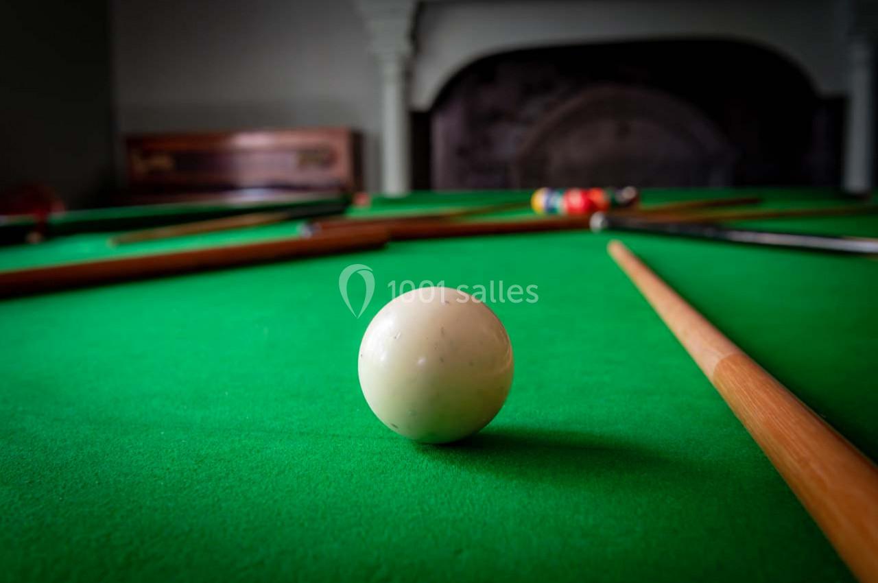 Bille blanche de billard posée sur une table verte, entourée de queues et d'autres billes en arrière-plan flou.