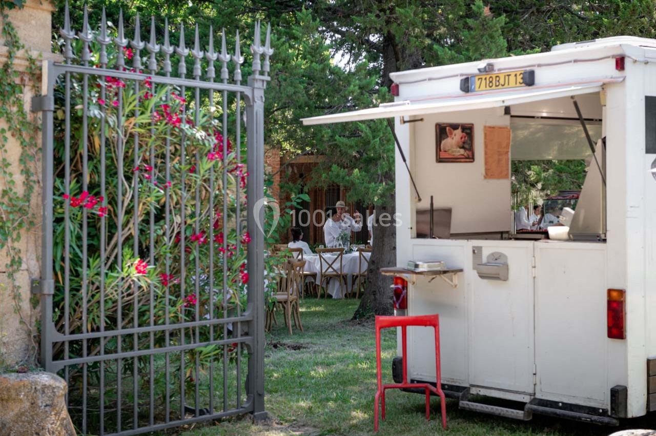 Camion de restauration blanche stationné près d'une grille en fer forgé, avec des tables dressées en arrière-plan.