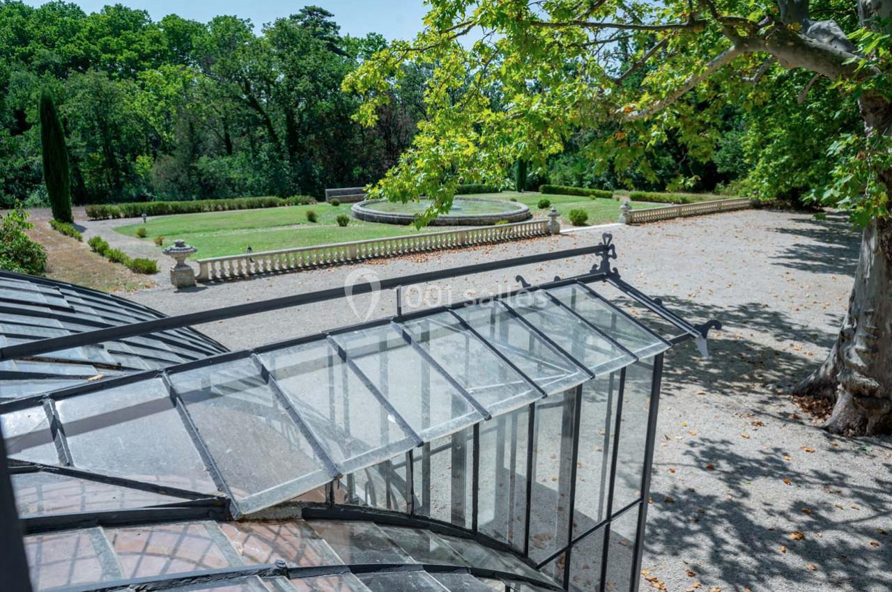 Vue d'un jardin avec pelouse, allées, bassin central et partie d'une verrière au premier plan.