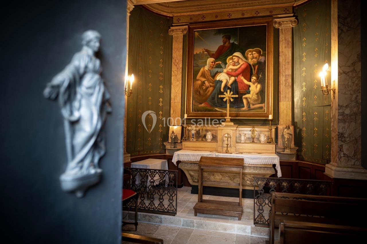 Petite chapelle avec un autel orné de statues, un tableau religieux en arrière-plan et des bancs en bois.