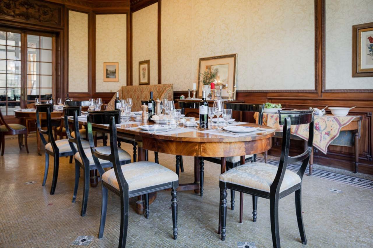 Salle à manger élégante avec tables en bois dressées, chaises rembourrées et décoration classique sur les murs.