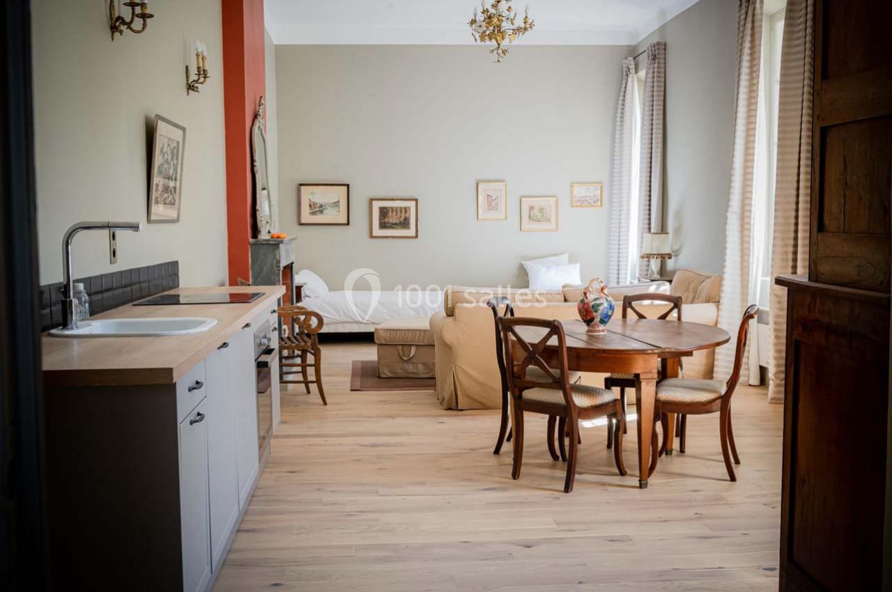 Pièce lumineuse avec coin cuisine, table en bois, canapé, lit simple et décorations murales.