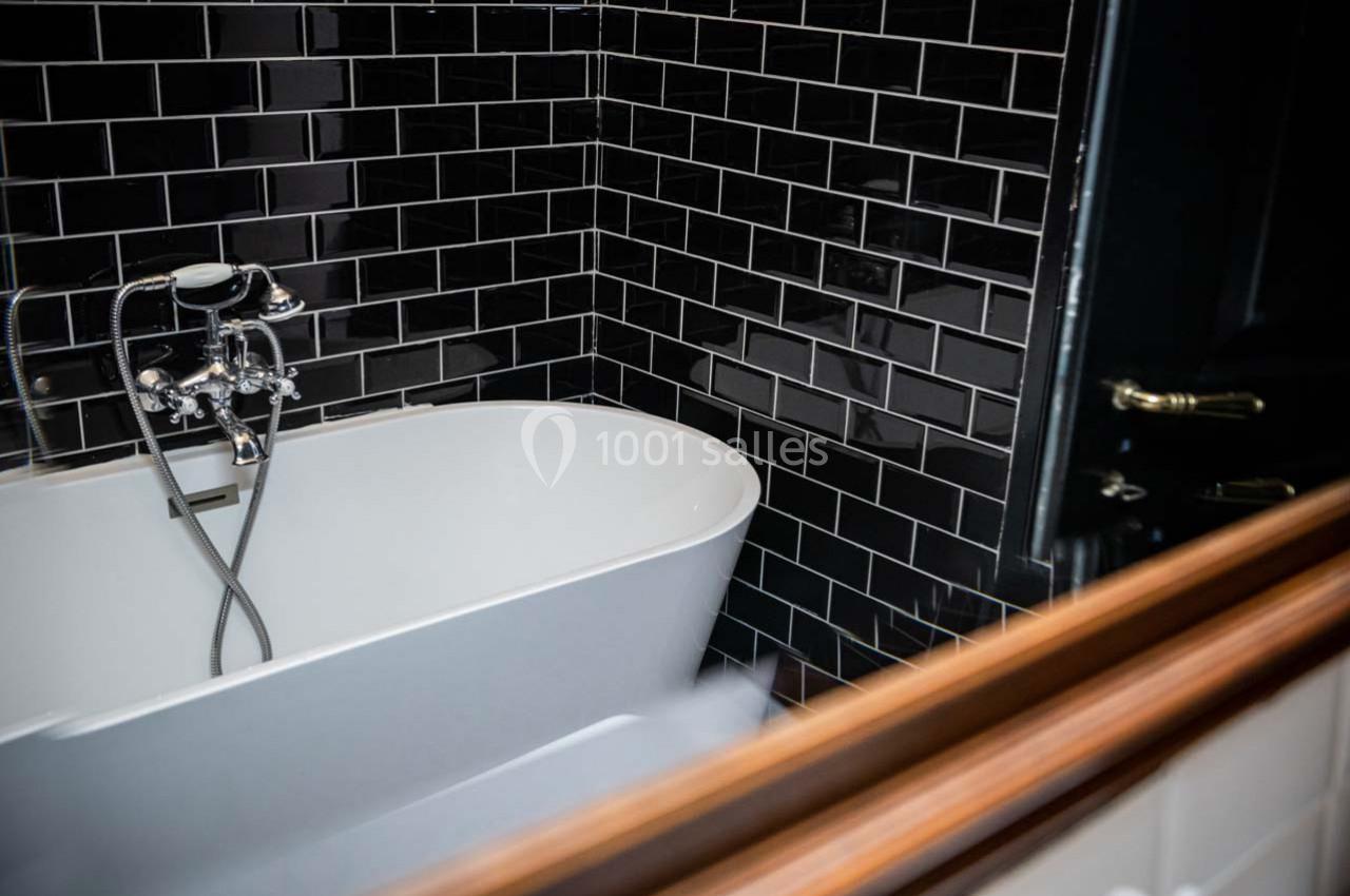 Baignoire blanche avec robinet chromé dans une salle de bain aux murs carrelés noirs brillants.