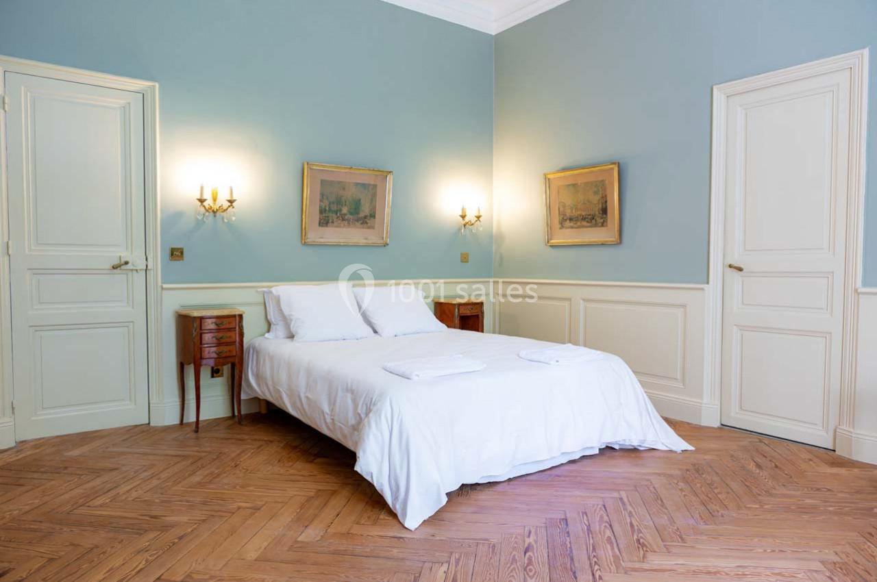 Chambre lumineuse avec murs bleus, parquet en bois, lit double avec draps blancs, deux tables de chevet et appliques murales.