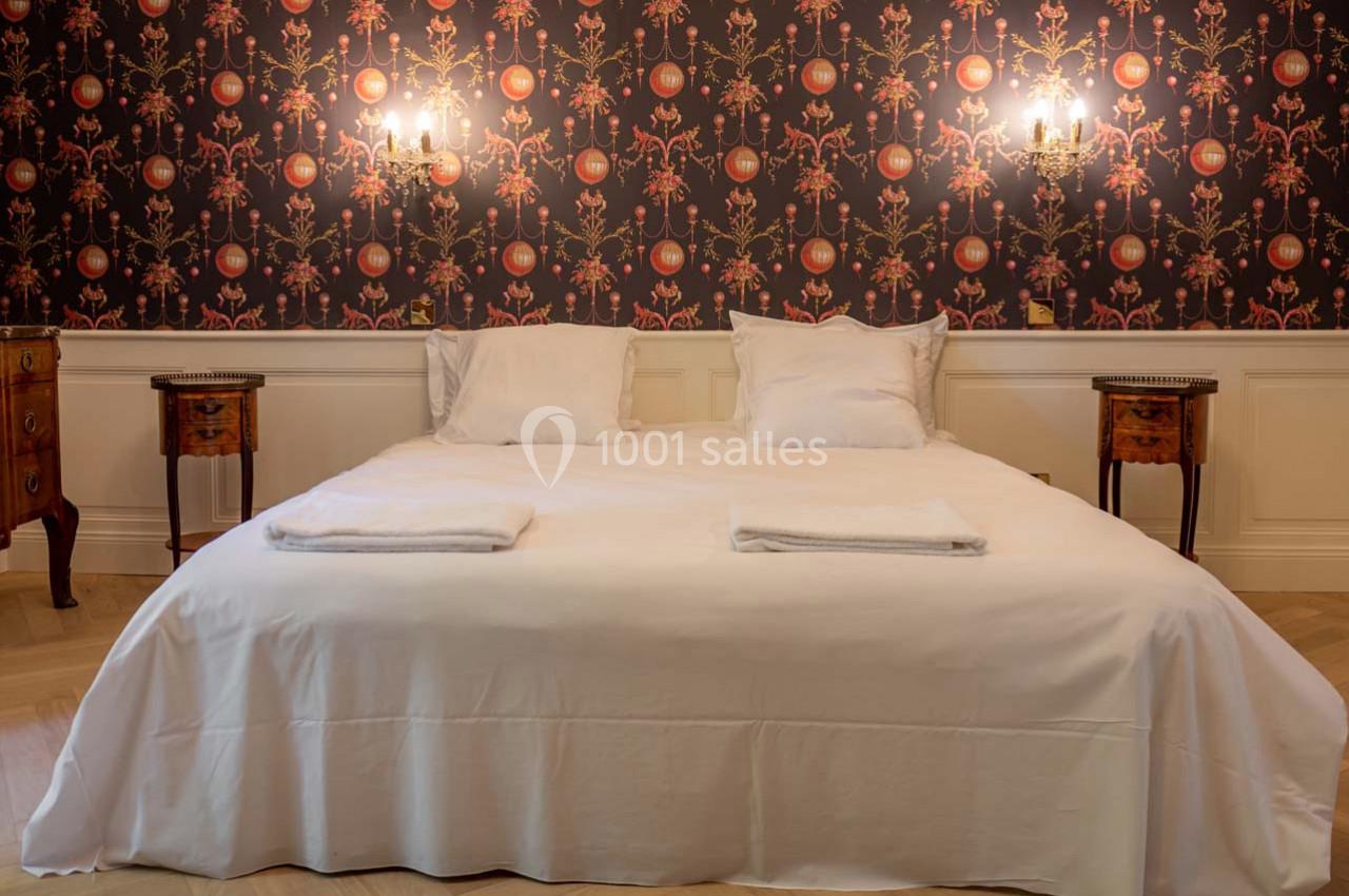 Lit double avec draps blancs, encadré par deux tables de chevet en bois, devant un mur à motif floral sombre.