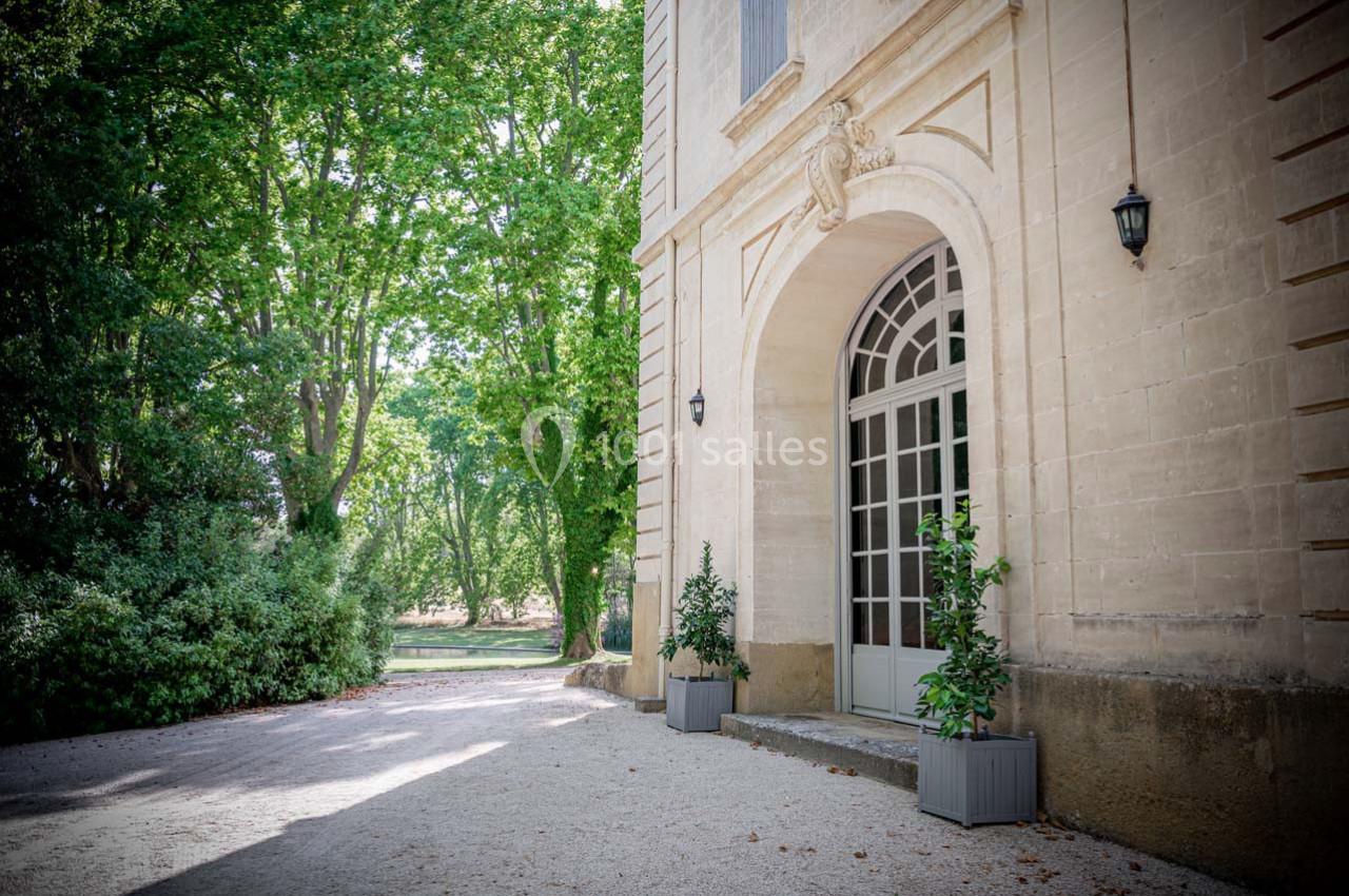 Façade d'un bâtiment en pierre avec une grande porte vitrée, entourée de verdure et de pots de plantes.