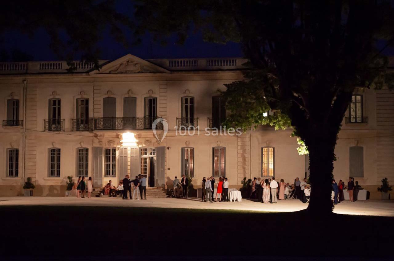 Groupe de personnes rassemblées devant un bâtiment historique éclairé la nuit, entouré d'arbres.