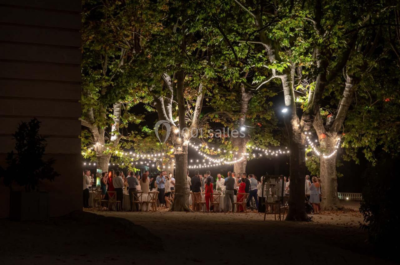 Groupe de personnes rassemblées sous des guirlandes lumineuses dans un jardin arboré, en soirée.