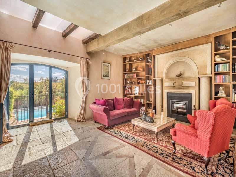 Salon lumineux avec cheminée, canapés rouges, étagères en bois, grandes fenêtres donnant sur une piscine extérieure.