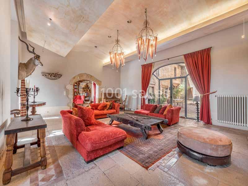 Salon spacieux avec canapés rouges, table basse en bois, grandes fenêtres et lustres suspendus.