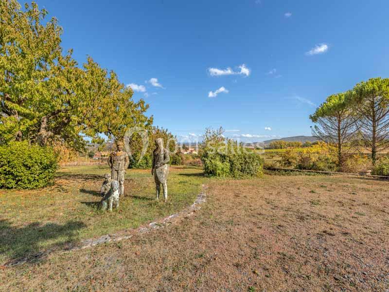 Deux statues humaines et un chien dans un parc verdoyant sous un ciel bleu avec des arbres en arrière-plan.