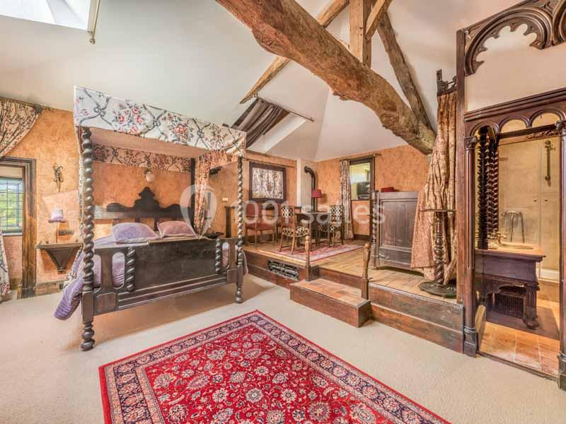 Chambre rustique avec lit à baldaquin, poutres apparentes, tapis rouge et mobilier en bois ancien.