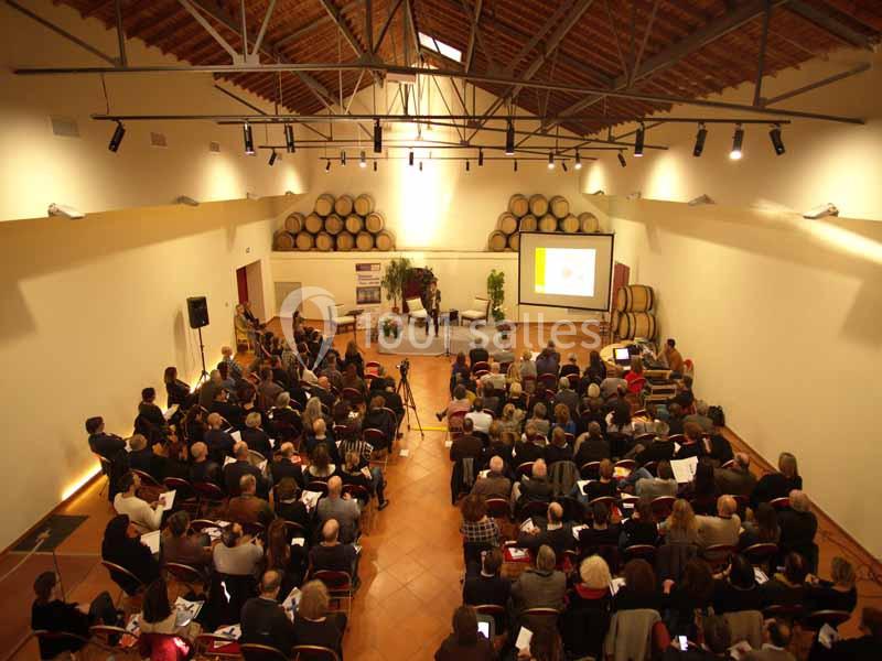 Salle de conférence avec un public assis, un intervenant sur scène et une présentation projetée sur écran.
