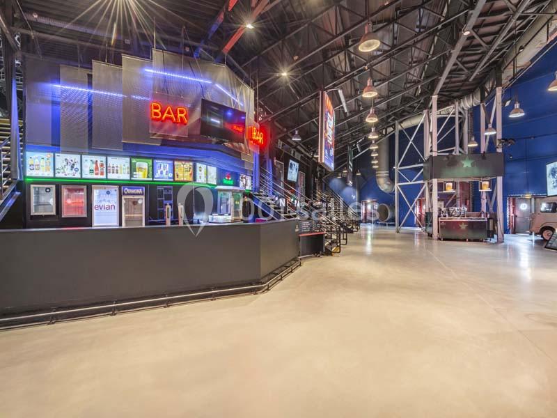 Intérieur d'un espace moderne avec un bar lumineux, des escaliers métalliques et un sol en béton poli.