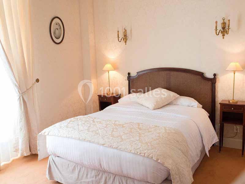 Lit double avec tête de lit en bois, couvert d'une couette claire, entouré de tables de chevet et lampes dans une chambre…