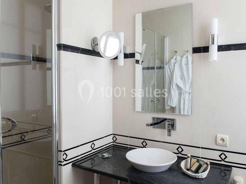 Salle de bain moderne avec lavabo rond, miroir, éclairage mural et douche vitrée en arrière-plan.