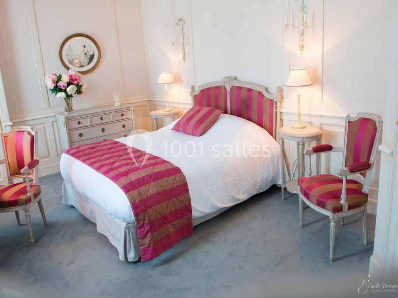 Chambre élégante avec lit double, mobilier classique en bois, et touches de rose et blanc dans la décoration.