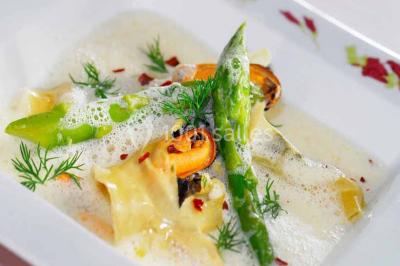 Assiette gastronomique avec légumes colorés, asperges, sauce crémeuse, tranche de viande et fleur comestible en décoration.