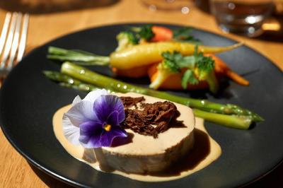 Assiette gastronomique avec légumes colorés, asperges, sauce crémeuse, tranche de viande et fleur comestible en décoration.