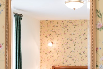 Chambre avec un lit double, draps blancs, coussins verts, deux tables de chevet et poutres apparentes au plafond.